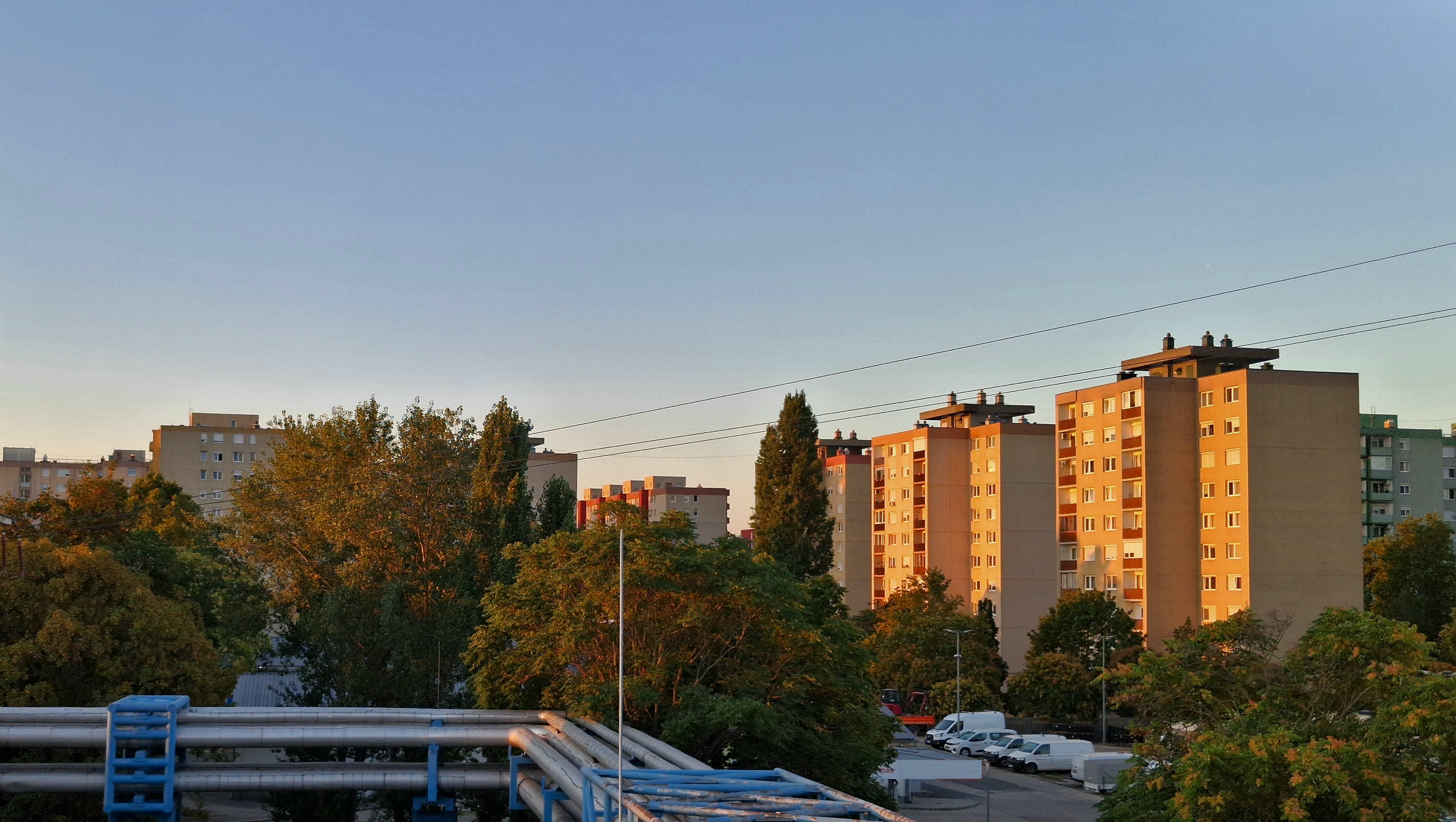 illusztráció a fűtésinduláshoz, a képen társasházak, fák és fűtéscsövek láthatók
